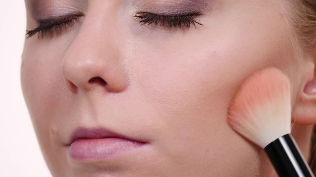 Woman face painting. Makeup artist applying blush bronzer with brush to model cheek. Cosmetic beauty procedures and makeover concept.  Slow motion