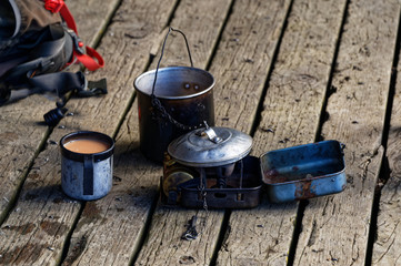 A pot or billy sits on a hut's veranda, there is a tin mug of milky tea that has just been brewed