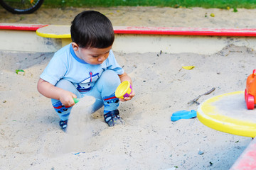Little latin boy playing with sand in the sandbox.