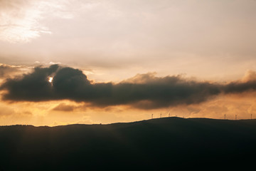 Panoramic of a landscape with mountains at sunset with windmills, the sun and clouds