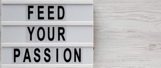 'Feed your passion' words on a lightbox on a white wooden background, top view. Overhead, from above, flat lay. Copy space.
