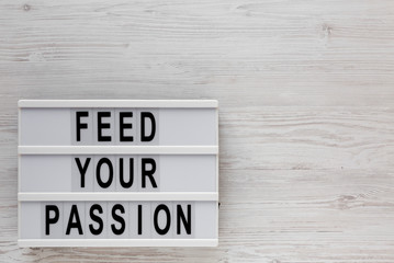 'Feed your passion' words on a lightbox on a white wooden surface, top view. Overhead, from above, flat lay. Space for text.