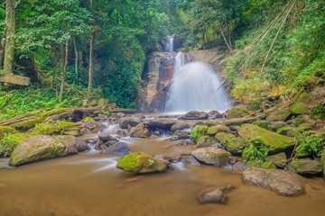view of silky waterfall flowing from the cliff around with many arch rocks and stream water with green forest background, Pu Muen Waterfall, Fang District, Chiang Mai, northern Thailand.