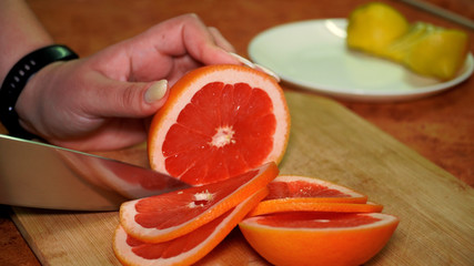 girl on a wooden board cuts with a knife a ripe juicy vitamin red grapefruit