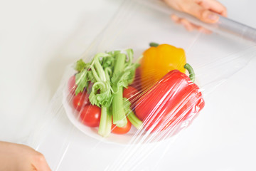 Woman using food film for food storage on a white table. Roll of transparent polyethylene food film for packing products.