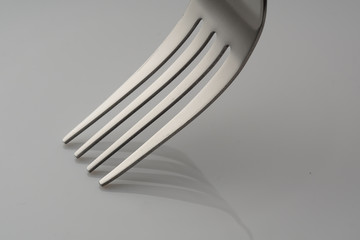 close up on shiny  fork with grey shadow over white plate
