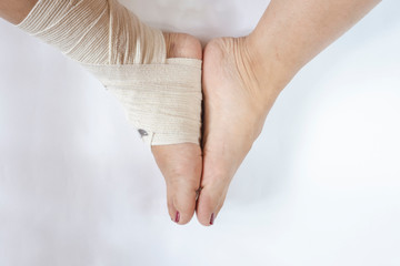 Woman's leg with sprained ankle with elastic bandage isolated on white background. Twisted bandaged ankle with bruise on white background.  Athlete runner training accident. - obrazy, fototapety, plakaty