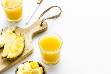 Pineapple juice in glass near sliced fruit on white background copy space