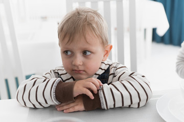 a little fair-haired boy sits at a light table and looks away in thought 