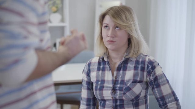 Close-up portrait of scared Caucasian young woman looking at clenched fist of husband. Beautiful wife afraid of tyranny of spouse. Relationship problems, tyranny, despotism.