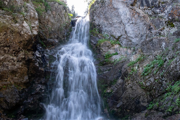Naklejka na ściany i meble Mountain tourism, hiking. Beautiful landscape with small waterfall among rocky mountains.