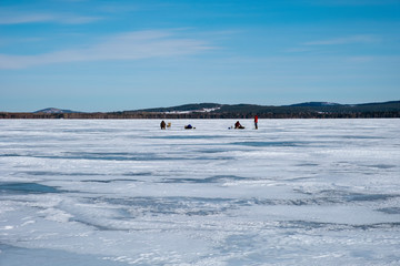 Winter landscape of frozen lake with silhouettes of fishermans  on ice.