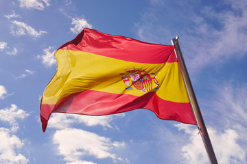 Flag of Spain waving in the wind in front of a blue sunny sky with clouds. Spanish flag in high resolution, concept for travel and tourism.