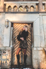 Girl in a colorful scarf is standing on the porch of an old wooden house. Autumn time.