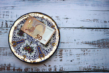 Fifty euro banknote on a beautiful decorative ornamental plate on wooden table