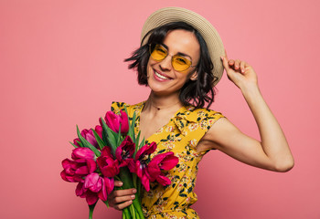 The portrait of a happy excited gorgeous young woman in stylish wear is posing with a freshness bunch of tulips. Mothers day. Women's holidays. Springtime.