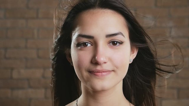 Happy young brunette girl with waving hair smiling in a brick studio in slo-mo