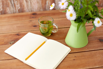 eco and organic concept - herbal tea, notebook with pencil and flowers in green jug on table