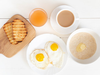 Oatmeal, eggs, juice, tea and toast. The concept of Breakfast. Top view with copy space on a white wooden table