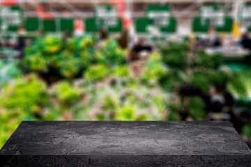 Black stone surface on blurry background of green vegetables in store.