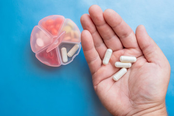 Closeup of man's hand with white pills in his hand. Blue background. Cure concept.
