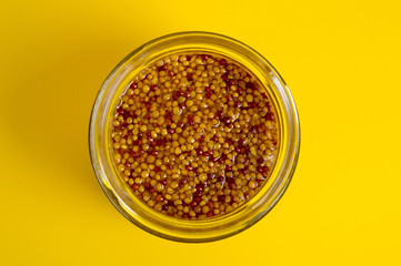 French mustard in a glass jar, shot on a yellow background. Background for seasoning and nutrition.