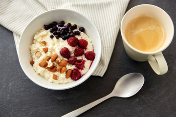 food and breakfast concept - porridge in bowl with wild berries, almond nuts, spoon and cup of coffee on slate stone table