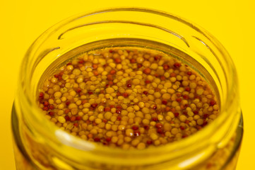 French mustard in a glass jar, shot on a yellow background. Background for seasoning and nutrition.
