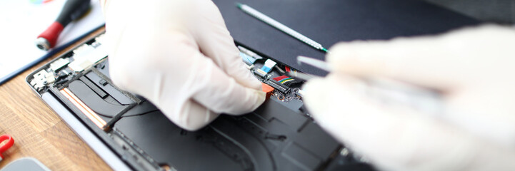 lose-up of male hands wearing protective gloves holding tweezers and making analysis of computer productivity. Gadgets maintenance service. Repairing of laptops hardware