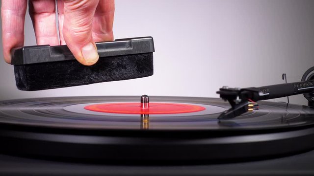Cinemagraph – Close POV video of a revolving vinyl LP, with a still image of a man’s hand holding a dust cleaning tool above the turntable. 