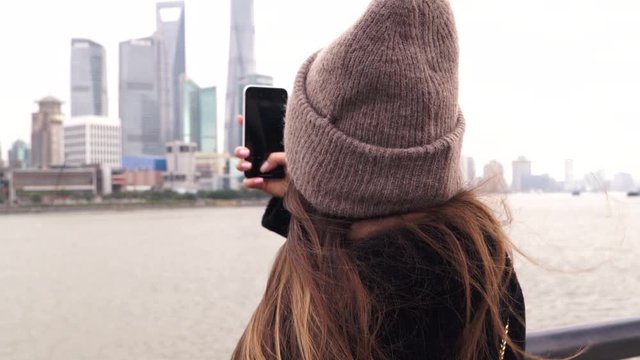 Tourist girl takes photo of skyscrapers at Waitan embankment of Shanghai