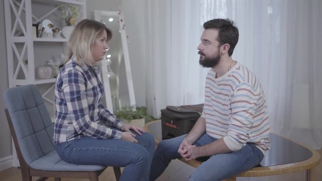 Nervous young woman yelling and hitting bearded husband with finger. Angry wife scolding husband indoors. Relationship problems, lifestyle, marriage, breakup, conflict, divorce.