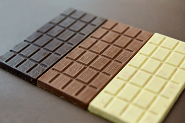 sweets, confectionery and food concept - milk, dark and white chocolate bars on brown background