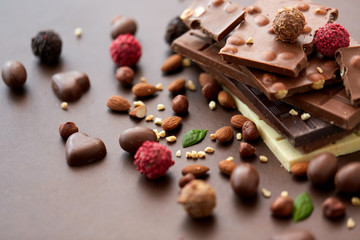 sweets, confectionery and food concept - close up of different chocolate bars, candies and nuts on brown background