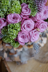 Beautiful spring bouquet close-up with pink roses and green carnations, decorated with feathers and birch bark. 