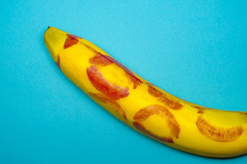 Red lipstick on a yellow banana on a blue background. Oral sex concept.