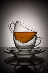 Two glass cups with tea and saucer with reflection, against the background of a white and black...