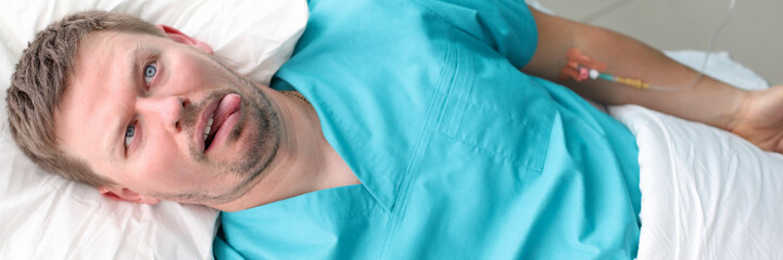 Person lying in bed showing grimace on face. Fun facial expression of human in medical center or private clinic. Humorous personage sticking tongue out