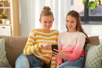 people, technology and friendship concept - happy teenage girls with smartphone sitting on sofa at home