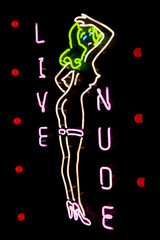 Nighttime view of glowing sign for live nude eriotic show featuring a woman with green hair outdoors 