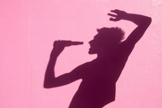 Shadow Of Dancing Spring Breaker Holding A Bottle To His Open Mouth With Bright Sunny Pink Wall Copy Space