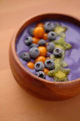 Smoothies of violet color from banana and currant, on top of a blackberry, physalis and kiwi berry. Smoothies in a wooden bowl.