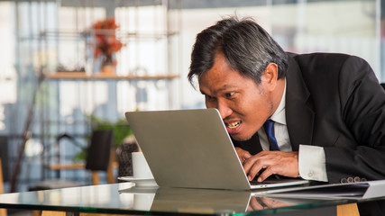Fototapeta premium Close up crazy middle Asian businessman typing a laptop on table in coffee shop
