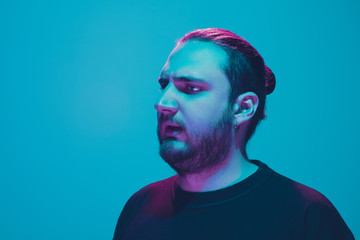 Portrait of a guy with colorful neon light on blue studio background. Male model with calm and serious mood. Facial expression, cyberpunk, millenials lifestyle and look like. Future, technologies.