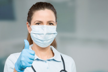 female doctor with medical face mask and medical gloves shows thumbs up 