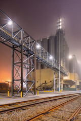 Foggy night scene with rails and pipeline overpass at petrochemical production plant, Port of Antwerp.