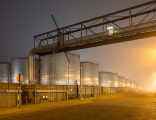 Night scene with large silo and pipeline overpass at petrochemical production plant, Port of Antwerp.