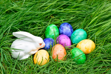 Cute ceramic bunny rabbit with colorful of eggs decoration on green grass in the garden background at spring or summer season. Happy easter day and holiday concept. 