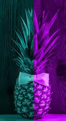Neon pineapple with bow tie flatlay turquoise duotone colors background. Tropical fruit wallpaper, vegan food vertical banner. Minimal social media creative top view. Minimalism style, trendy toning.
