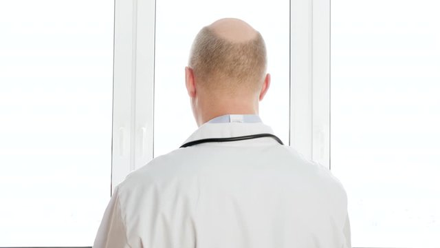 Traumatologist looking x-ray of spine bones on window light background on clinic. Back view surgeon watching backbones x-ray in hospital